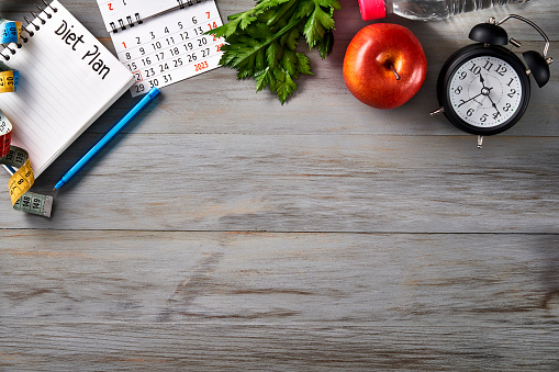 Top view of Clock, notepad with pen, calendar, tape measure, water bottle, apple and smart watch on a table with copy space