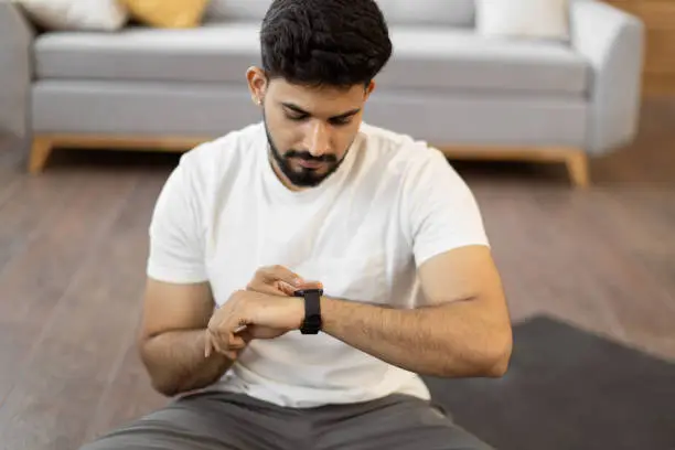 Photo of Arabic man setting heart-rate watch during home training