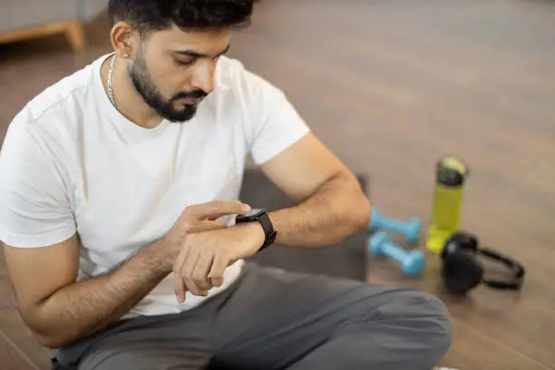 Photo of Arabic man setting heart-rate watch during home training