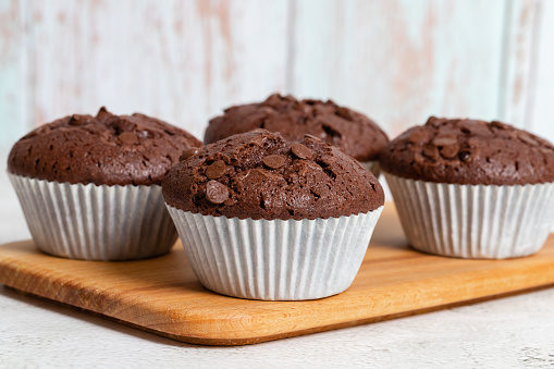 Plain chocolate muffins with chocolate chips in white paper cups, close-up view, copy space