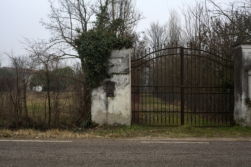 Closed  gate with a votive niche by the edge of a road in the italian countryside on a cloudy day