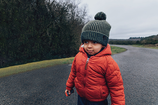 african american kid wearing wool cap and jacket walking along the road in nature in a cold winter day