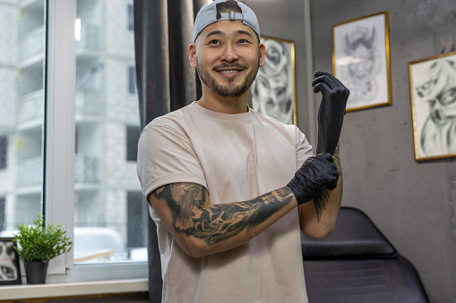 In the tattoo salon. Young asian man putting on gloves