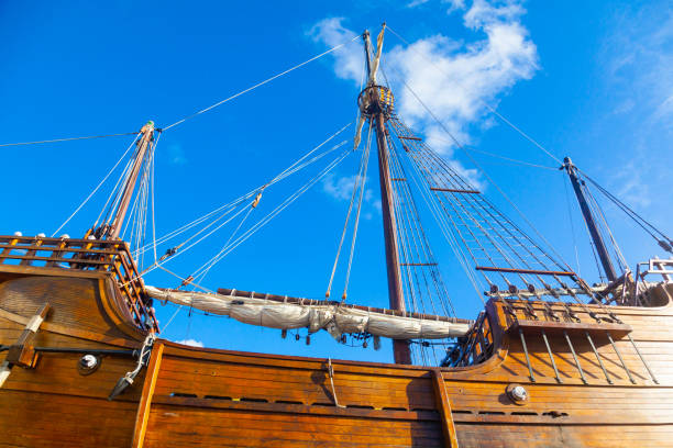 istock An old wooden caravel ship with folded sails against a blue sky with white clouds. 1476251578