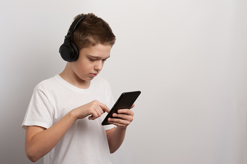 A boy with a tablet and headphones chooses his favorite music from a playlist