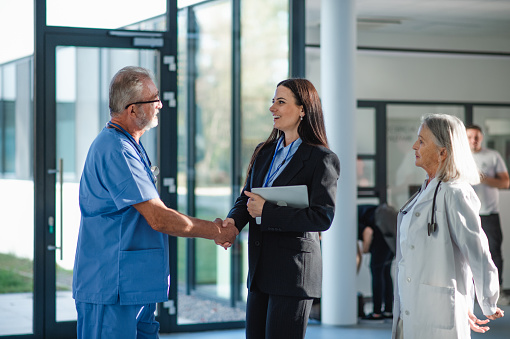 Young business woman shaking hand with elderly doctor in a hospital room.