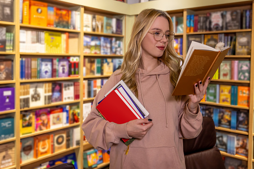 In library. Pretty blonde woman standing with books in library