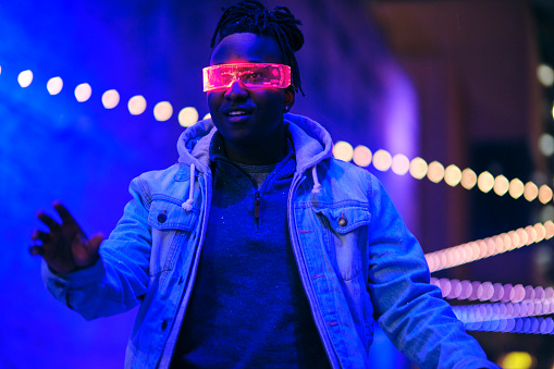 A young man wearing virtual glasses at night in a city with blurred lights.