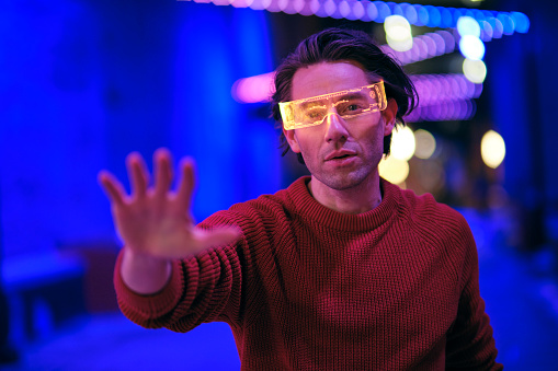 A young man wearing virtual glasses at night in a city with blurred lights.