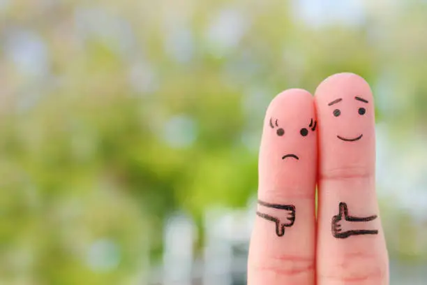 Photo of Fingers art of couple. Woman showing thumbs up and man showing thumbs down. Concept of disagreement in family.