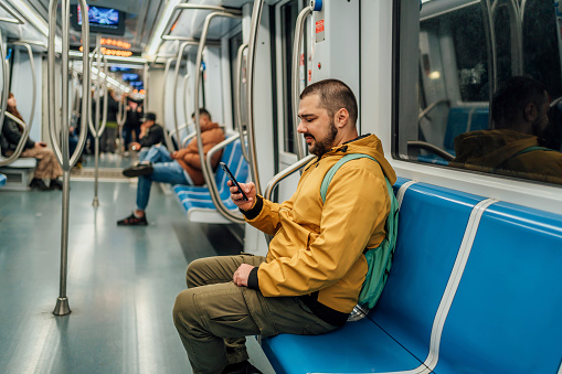 Young cheerful man using smartphone on a subway train