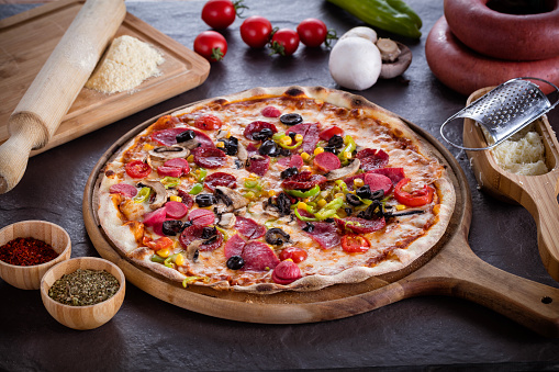 Delicious mixed pizza with tomatoes, olives , mozzarella, pepper, olive, corn, sausage, bacon. Italian food image.