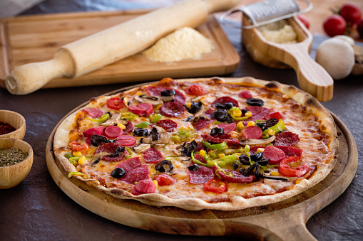 Delicious mixed pizza with tomatoes, olives , mozzarella, pepper, olive, corn, sausage, bacon. Italian food image.