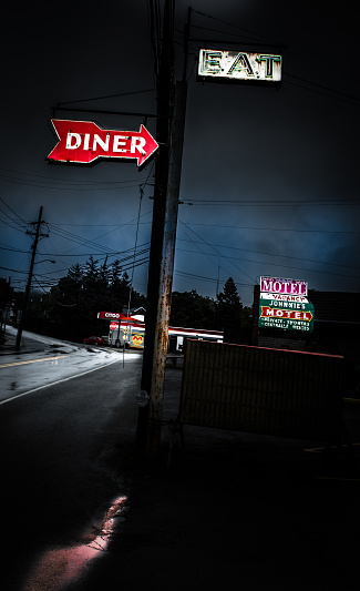 McConnellsburg, Pennsylvania - USA: Noir, night-time image of illuminated, neon signs -  DINER, EAT, MOTEL. Illuminated Citgo station in the distance with bluish dark sky. Reflections on road and water puddle.