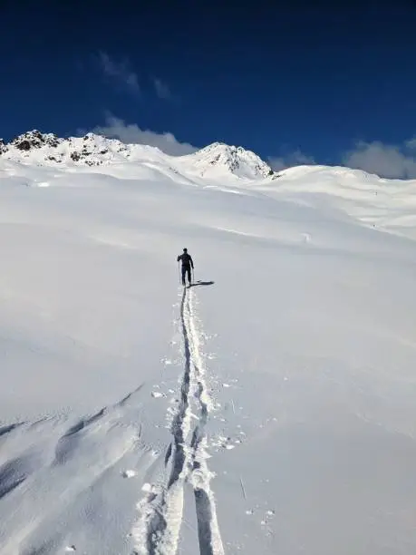 Ski tourers make a lonely track through the deep snow in the mountains above Davos. Ski mountaineering in the Swiss Alps. Skitouring, ski tour, skitour, skimo. High quality photo