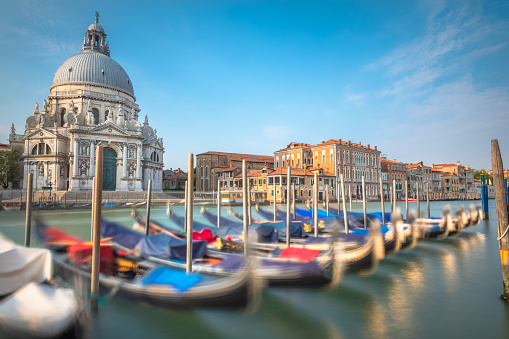 Gondolas in a row on Grand Canal and Santa Maria Della Salute Cathedral in Venice at peaceful sunrise, Italy