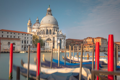 Gondolas in a row on Grand Canal and Santa Maria Della Salute Cathedral in Venice at peaceful sunrise, Italy