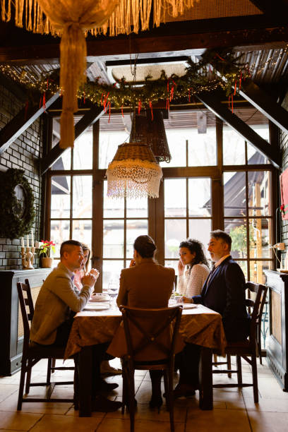 A medium view of three friends messing about in a cafe, two of them have stuck sweet potato and French fries in their mouths as if fangs. They are dressed in a trendy fashion and have burgers and other food in front of them.Videos of this scenario are also accessible.
