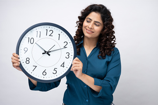 It's 10:10 o'clock. Portrait of positive cheerful woman having round clock in hands looking at camera on white background