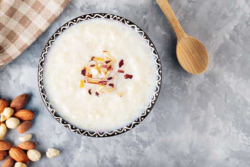 Indian kheer rice pudding with nuts on concrete. Bowl with rice pudding and a wooden spoon on a gray background. Top view