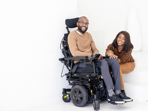 Happy Black couple at home portrait. Man is sitting in a wheelchair while the woman is holding his hand sitting on stairs
