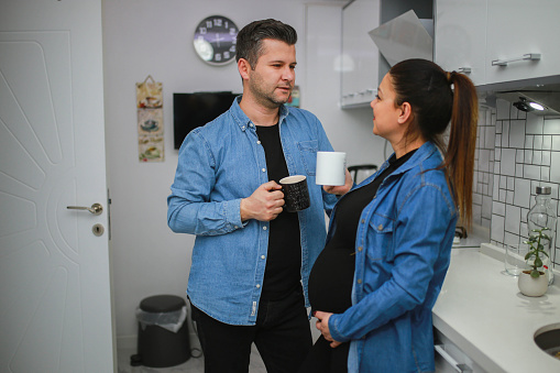 happy pregnant young woman and her husband drinking coffee together in the kitchen. newborn concept