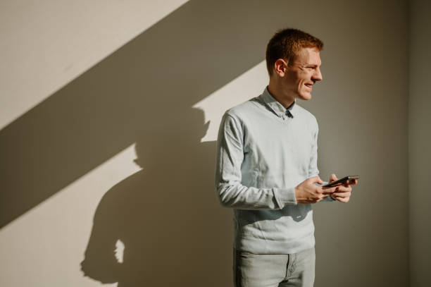 istock Redhead businessman using smartphone while standing over a white wall in an office 1476300291