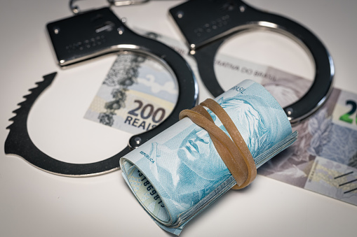 Handcuffs lying on the table next to a bundle of Brazilian money, Concept, Criminal activity in Brazil, Illegal business, Black market
