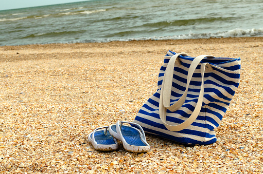 Beach bag and slippers on the beach by the sea. Things for recreation