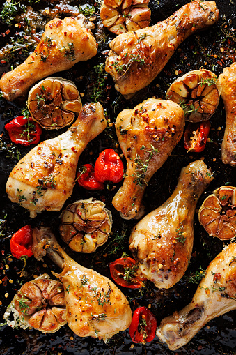 Spicy roasted chicken legs, drumsticks seasoned with garlic, hot peppers and aromatic herbs on a black background, close-up