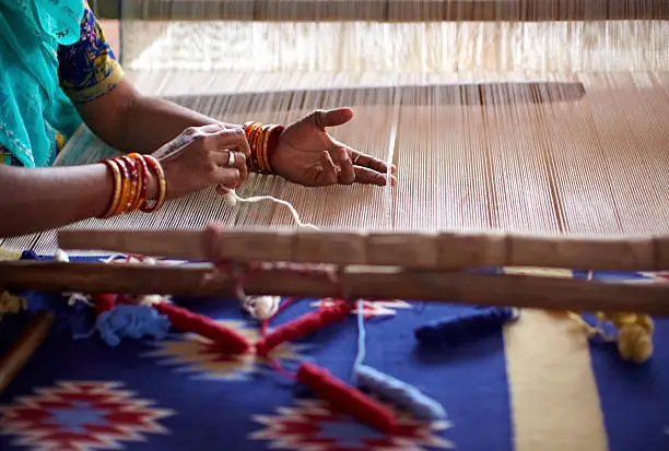 Woman waving a carpet on a manual loom in India