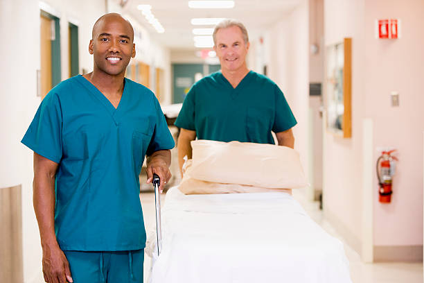Two Orderlies Pushing An Empty Bed Down A Hospital Corridor Two Orderlies Pushing An Empty Bed Down A Hospital Corridor Smiling porter photos stock pictures, royalty-free photos & images