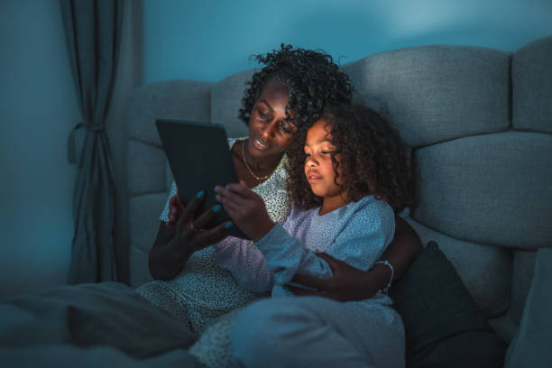 istock Lovely Black Mother And Multiracial Daughter Using A Digital Tablet At Night 1476341877