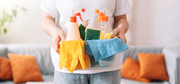 Girl holding in her hand cleaning products with rags and gloves in a plastic container.