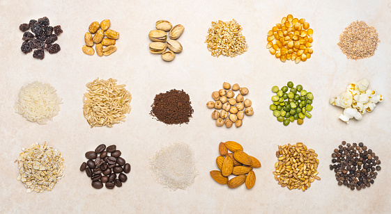 High angle view of healthy food ingredients , knolling-concept.
First row from left to right the ingredients are: raisin,  peanut,  pistachio, sesame, corn and bran. Second row from left to right: white rice, ground coffee, chickpea, green peas and popcorn.Third row from left to right: oatmeal, roasted coffee beans, sugar, almond, wheat and black pepper.