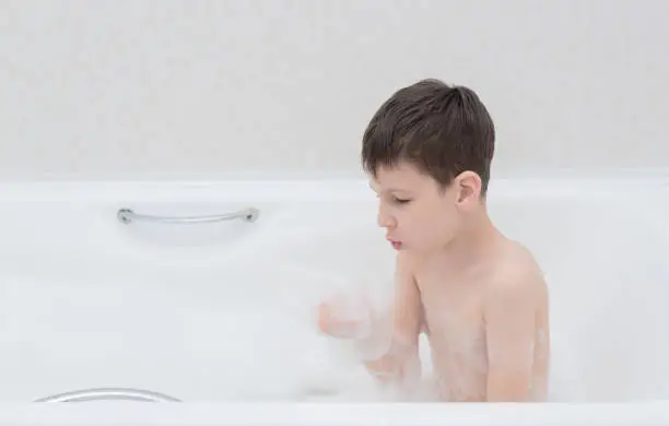 Photo of Happy boy takes a bath with lush foam playing with bubbles. Personal hygiene, healthcare concept