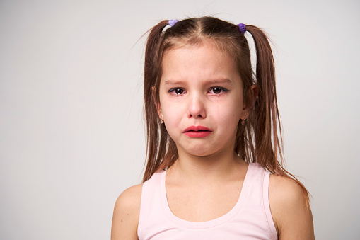 Crying child girl against white background with copy space. Portrait of a sad baby girl with tear drops on eyes, close-up