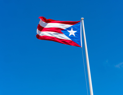 Flag of Chile flies in a strong wind against a bright blue sky with sun glare. Patriotic symbol of Chile, South America.