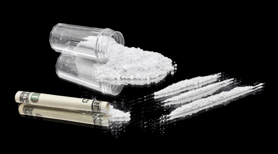 Three lines of cocaine beside a rolled up bill and vial of powder.