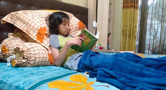 A little girl is relaxing on her bed and read favorite book in the bedroom.