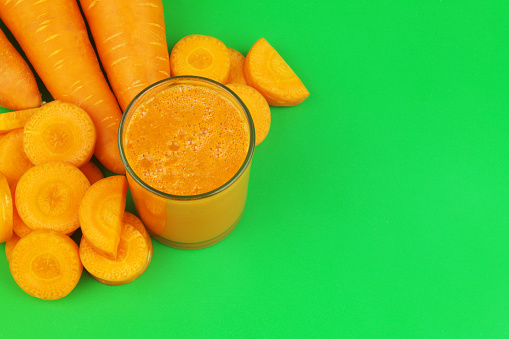 Fresh carrot juice and whole and sliced carrots on green background. Copy space for text.
