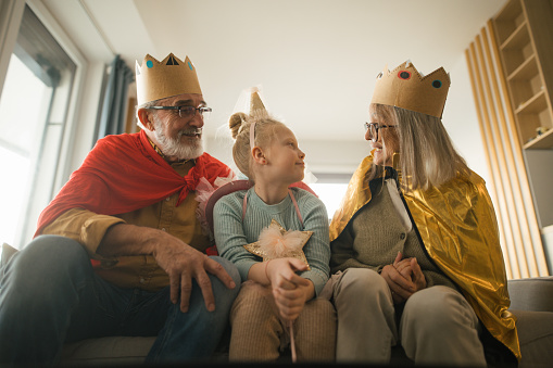 Grandparents playing with their little granddaughter, having costumes of king and queen.