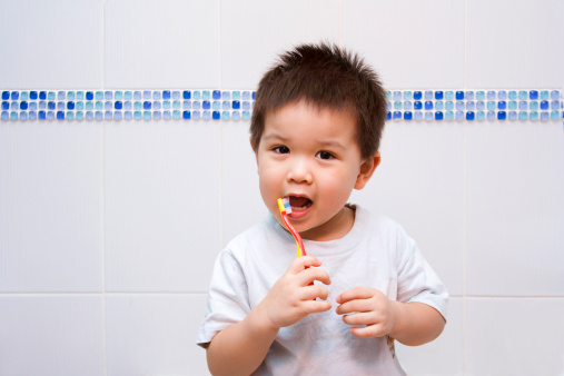 Little boy happily brushing his teeth in the bathroom. Behind him is a tiled wall with a border of modern bubble mosaic in various shades of blue.