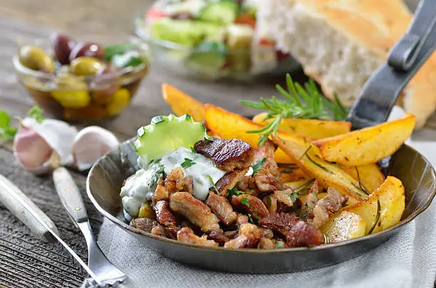 Greek pork gyros with tzatziki and fried potatoes, served with pitabread, salad and olives