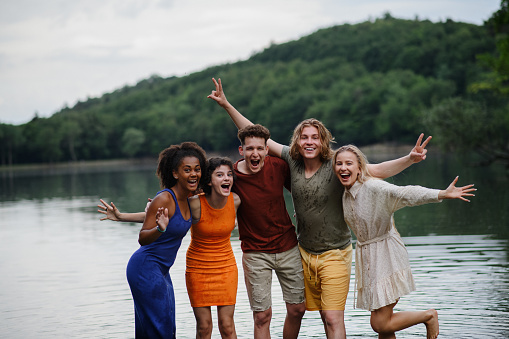 A multiracial group of young friends holding hands and standing in lake in summer.