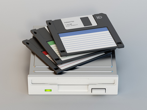 Generic HD floppy disks standing on floppy disk drive. Retro computer and data archive technology concept.