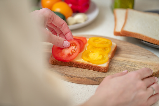 Woman making sandwich with a cheese and red and yellow tomatoes