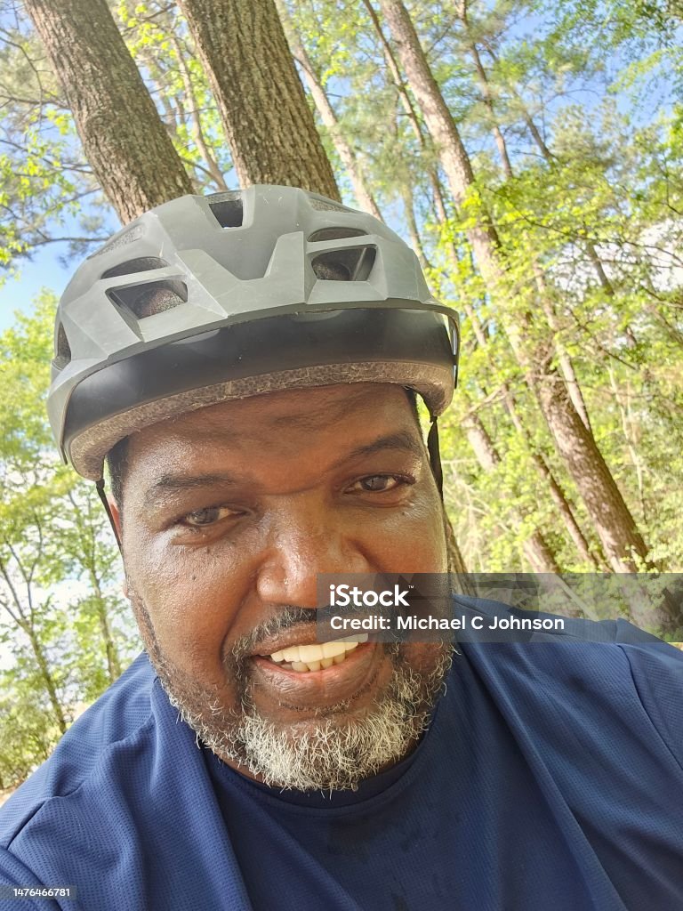 Close Up Middle Age Black Male Exercising Riding Bike Outdoors A Black male exercising riding a bike outdoors, wearing a biking helmet. Smiling under sun while working out to lose weight. Cycling Helmet Stock Photo