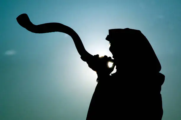 Silhouette of a Jewish man blowing a long shofar made from the horn of a kudu antelope at sunrise in Israel.