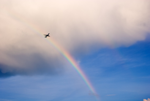 Airplane Flying Under Clouds With Double Rainbow